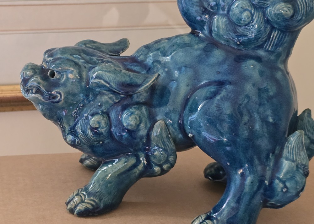 A Japanese glazed ceramic shishi guardian lion rendered in a rich turquoise blue glaze with a raised curling tail. View X