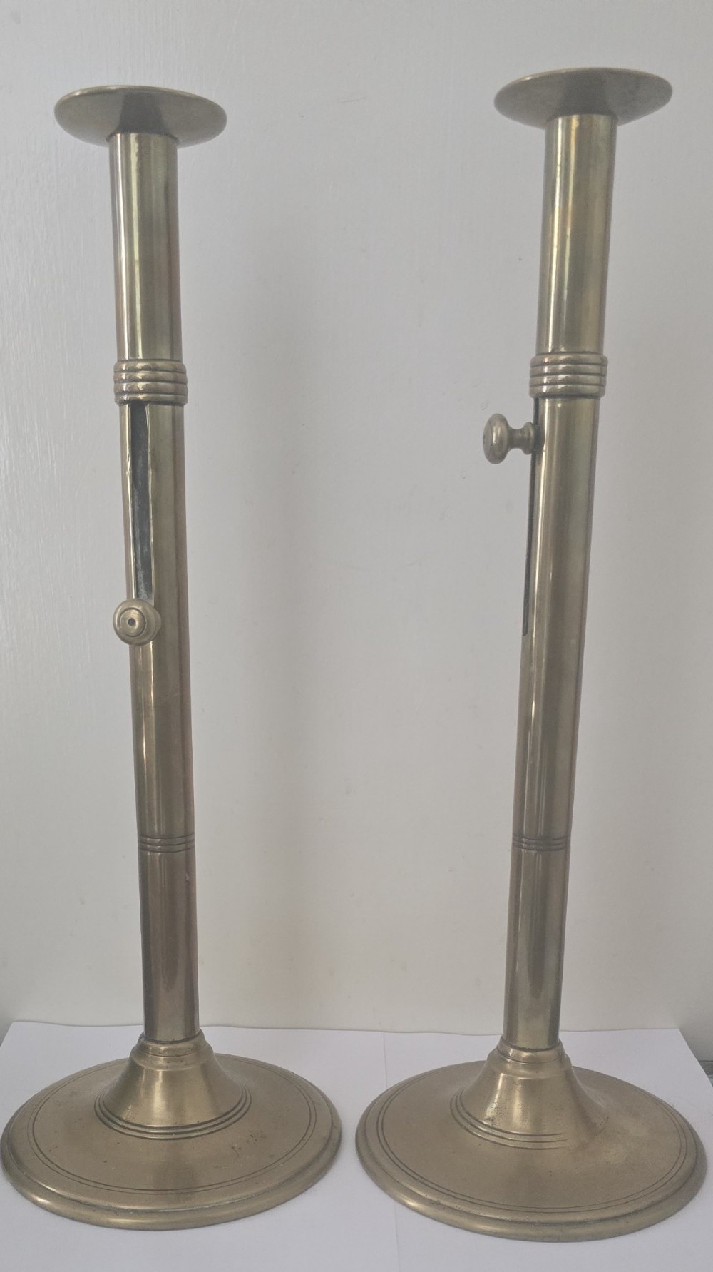 A pair of tall Georgian brass candlesticks featuring circular stepped bases, cylindrical stems, top wax pans, and side ejector push-up knobs.