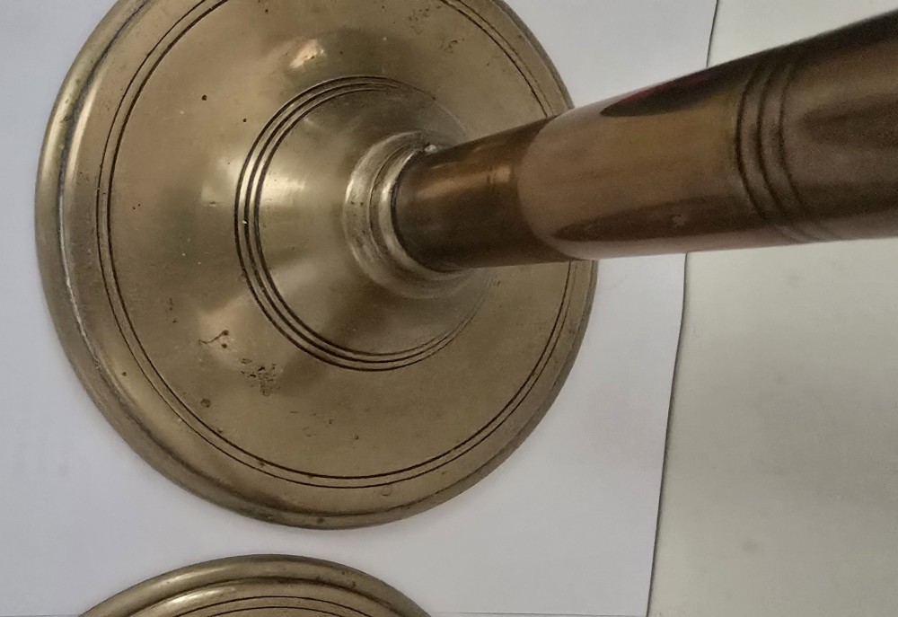 A pair of tall Georgian brass candlesticks featuring circular stepped bases, cylindrical stems, top wax pans, and side ejector push-up knobs. View VI