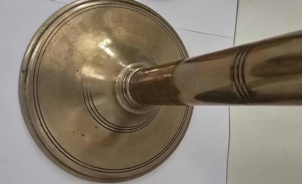 A pair of tall Georgian brass candlesticks featuring circular stepped bases, cylindrical stems, top wax pans, and side ejector push-up knobs. View VII