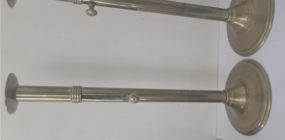 A pair of tall Georgian brass candlesticks featuring circular stepped bases, cylindrical stems, top wax pans, and side ejector push-up knobs. View X