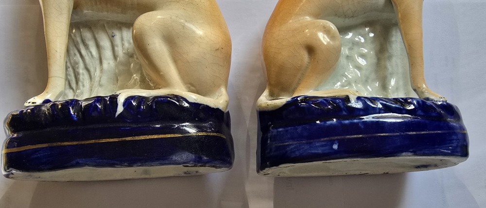 A pair of Victorian Staffordshire earthenware figurines depicting seated buff-coloured whippet dogs positioned on cobalt blue bases. View IX