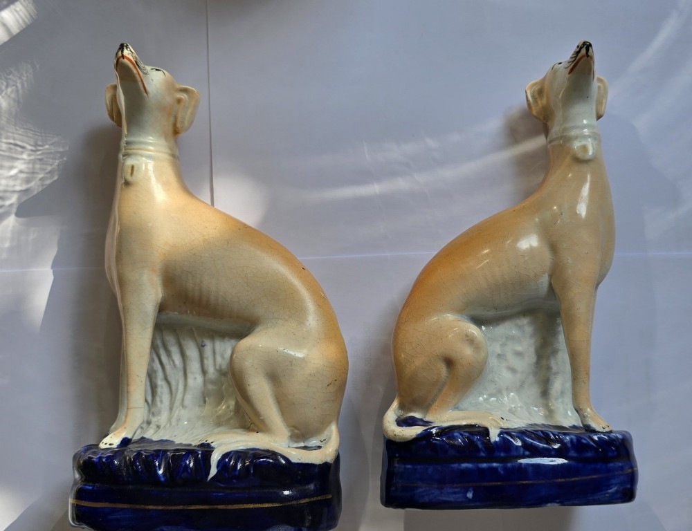 A pair of Victorian Staffordshire earthenware figurines depicting seated buff-coloured whippet dogs positioned on cobalt blue bases. View XIII