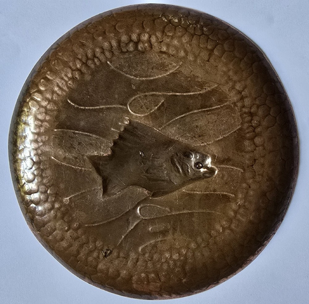 A circular hand-hammered copper visiting card tray featuring a central repousse fish motif surrounded by chased water lines and a spot-hammered rim. View VI
