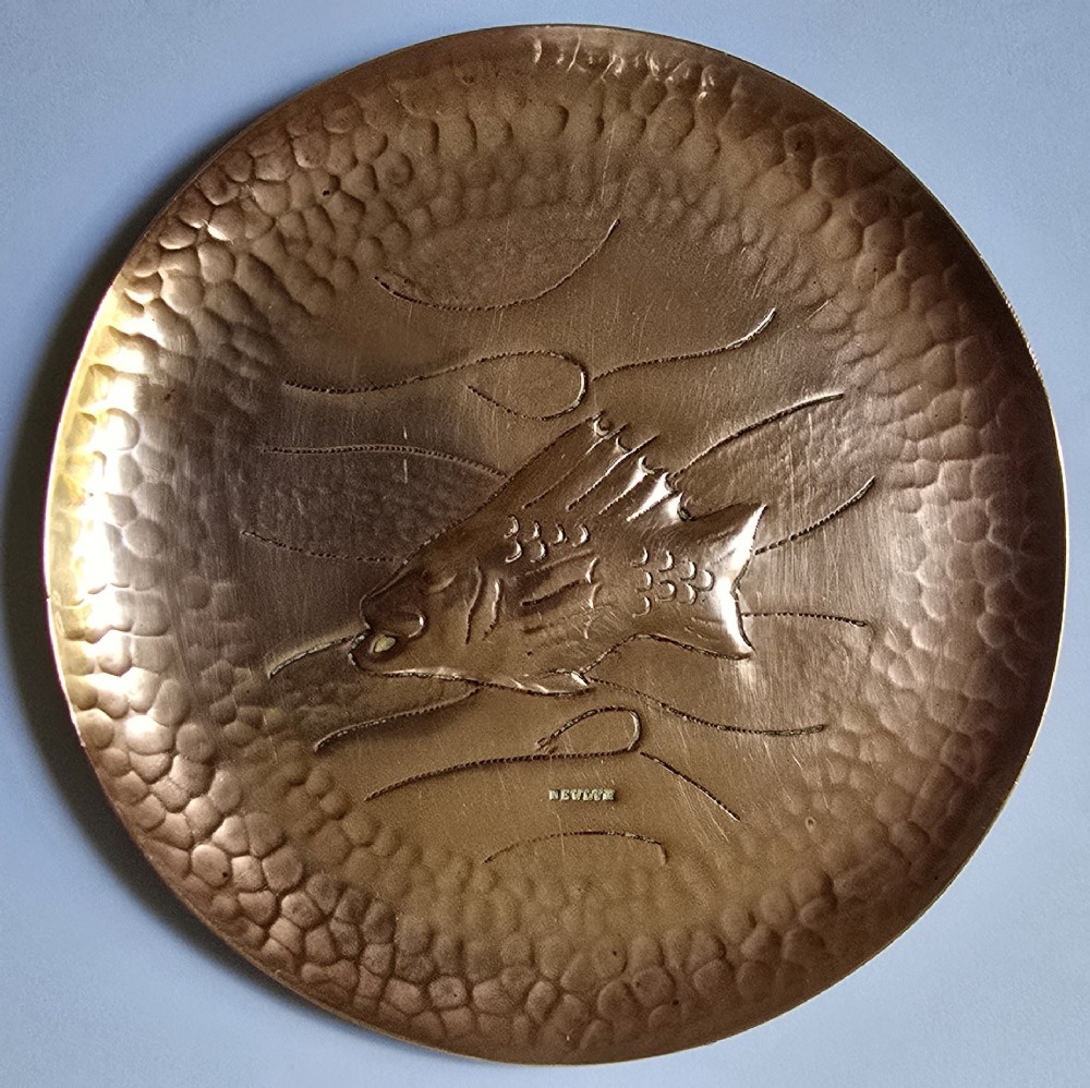 A circular hand-hammered copper visiting card tray featuring a central repousse fish motif surrounded by chased water lines and a spot-hammered rim. View IX