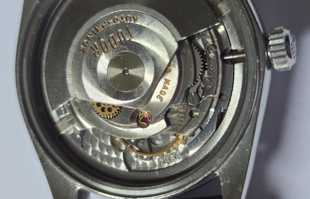A vintage Tudor Prince Oysterdate wristwatch with a stainless steel case, a black dial featuring baton hour markers, a date aperture at three oclock, and a dark brown leather strap. View XII