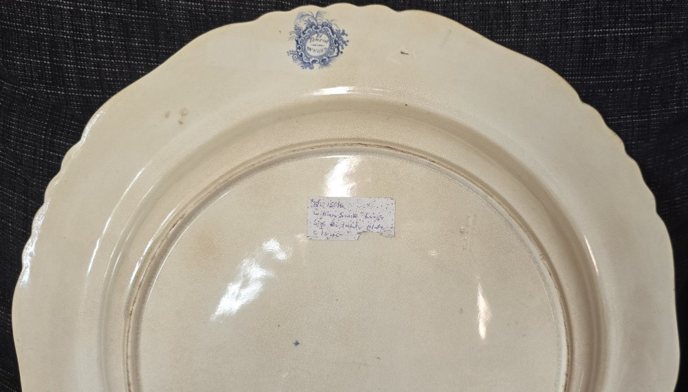 An antique circular earthenware plate featuring a blue transfer-printed central scene of Hannibal with an elephant and figures in a mountainous landscape, surrounded by an ornate scalloped floral border. View X