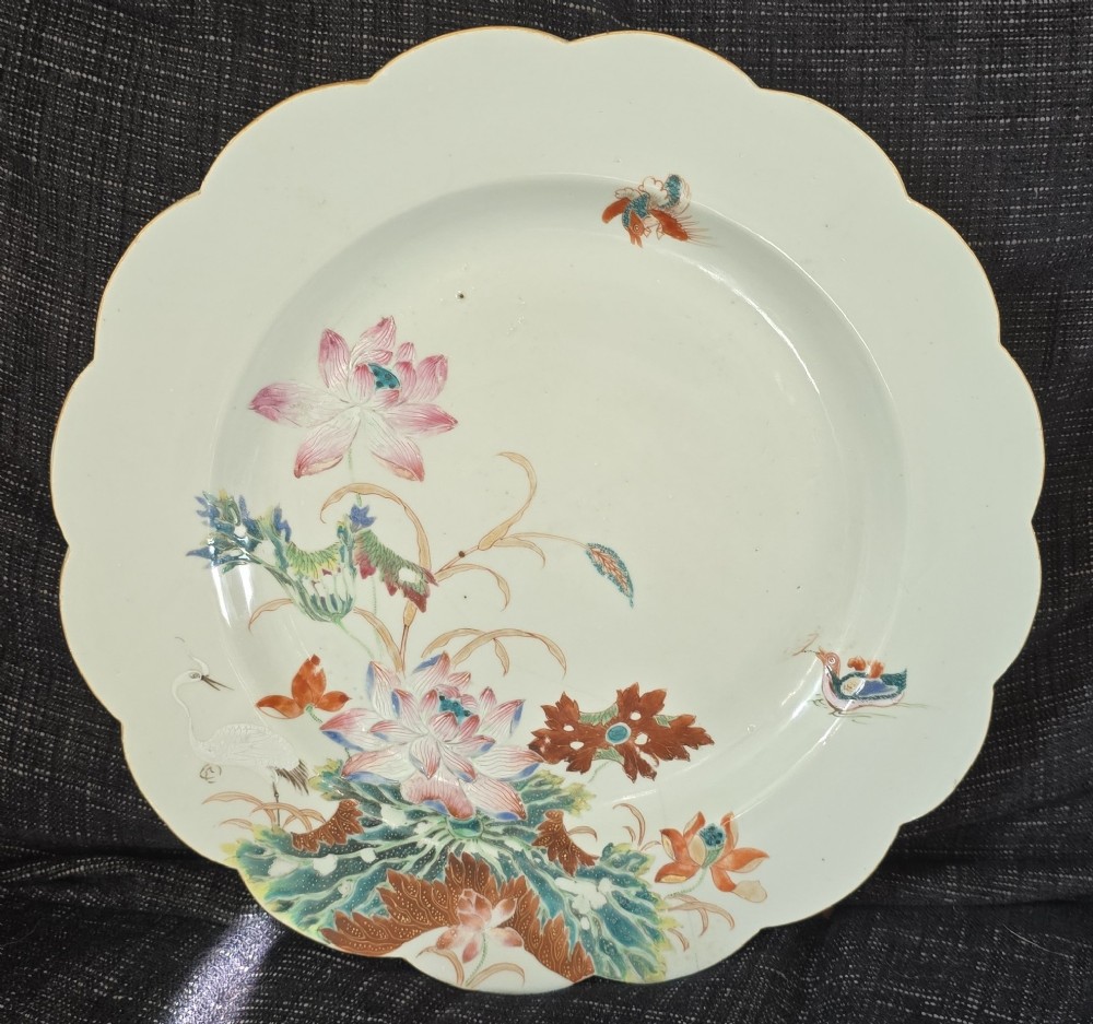 An antique circular off-white porcelain dish with a scalloped rim, hand-painted with pink lotus blossoms, foliage, a crane, and a waterfowl.