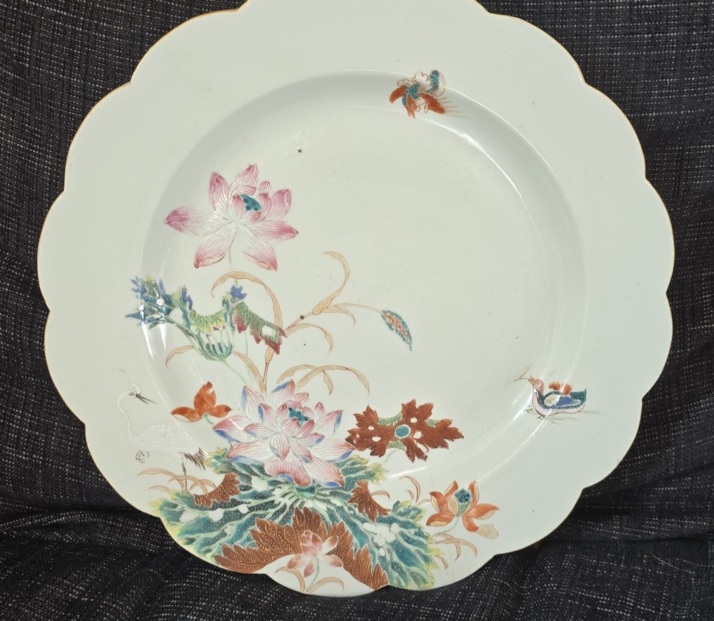 An antique circular off-white porcelain dish with a scalloped rim, hand-painted with pink lotus blossoms, foliage, a crane, and a waterfowl. View II