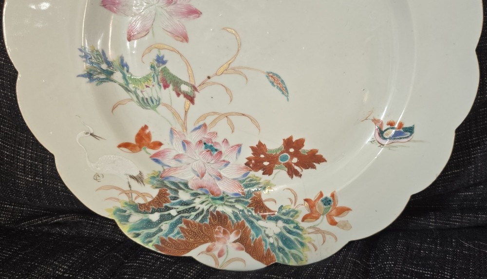 An antique circular off-white porcelain dish with a scalloped rim, hand-painted with pink lotus blossoms, foliage, a crane, and a waterfowl. View III
