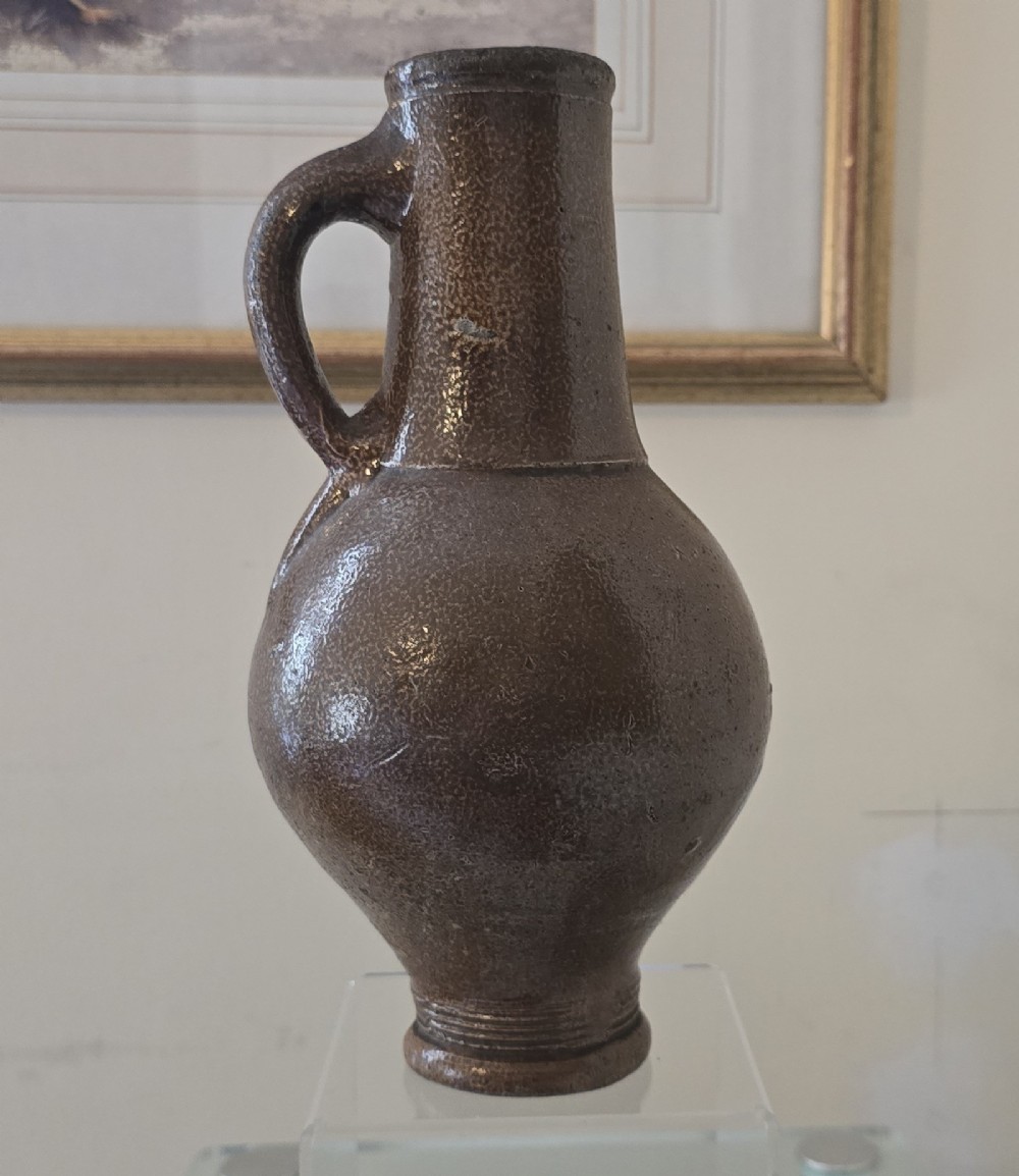 A 17th-century dark brown salt-glazed stoneware bottle featuring a bulbous body, narrow neck, turned base, and a single loop handle. View II