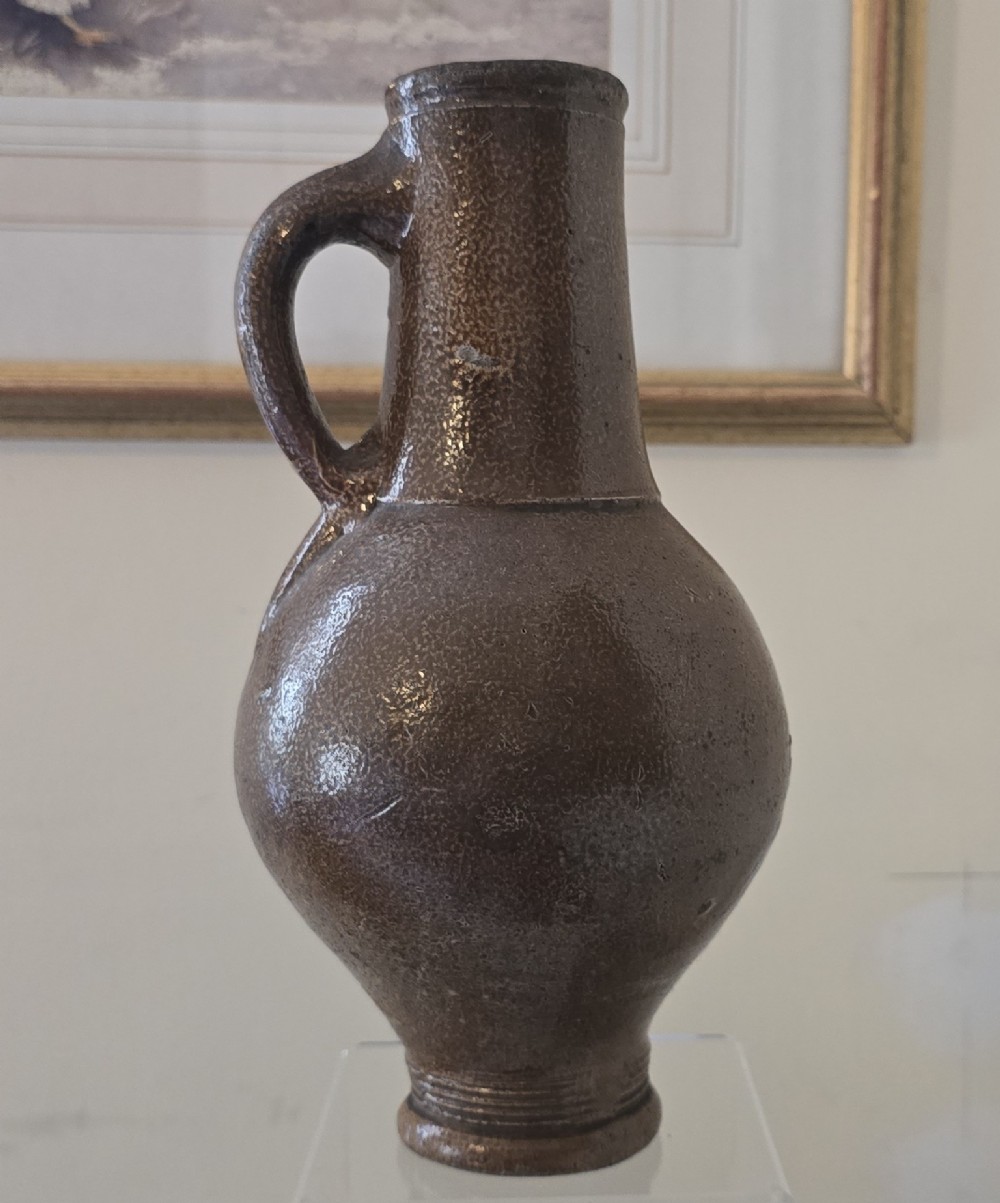 A 17th-century dark brown salt-glazed stoneware bottle featuring a bulbous body, narrow neck, turned base, and a single loop handle. View III