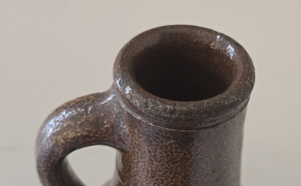 A 17th-century dark brown salt-glazed stoneware bottle featuring a bulbous body, narrow neck, turned base, and a single loop handle. View IV