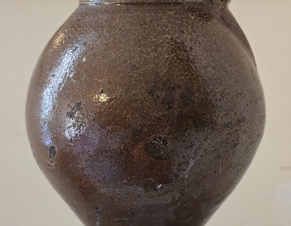 A 17th-century dark brown salt-glazed stoneware bottle featuring a bulbous body, narrow neck, turned base, and a single loop handle. View VII