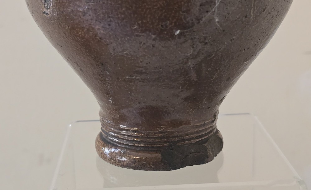 A 17th-century dark brown salt-glazed stoneware bottle featuring a bulbous body, narrow neck, turned base, and a single loop handle. View VIII