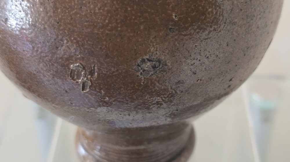 A 17th-century dark brown salt-glazed stoneware bottle featuring a bulbous body, narrow neck, turned base, and a single loop handle. View XI