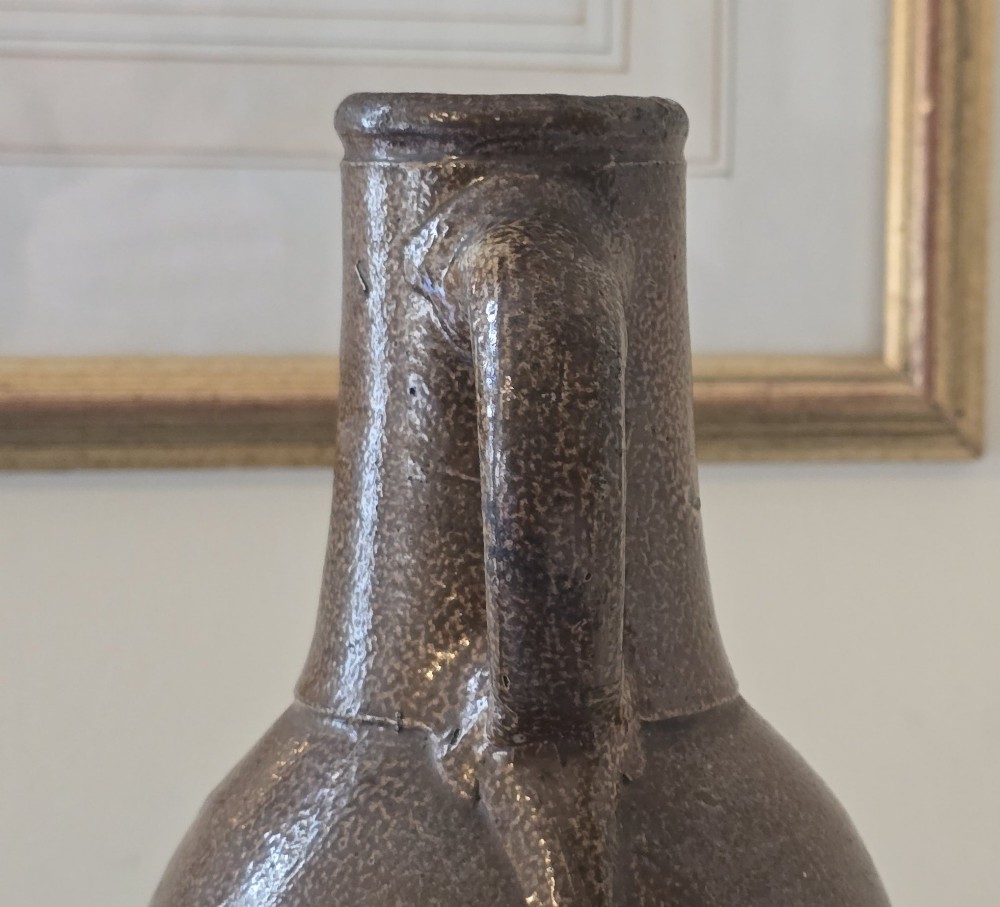 A 17th-century dark brown salt-glazed stoneware bottle featuring a bulbous body, narrow neck, turned base, and a single loop handle. View XII