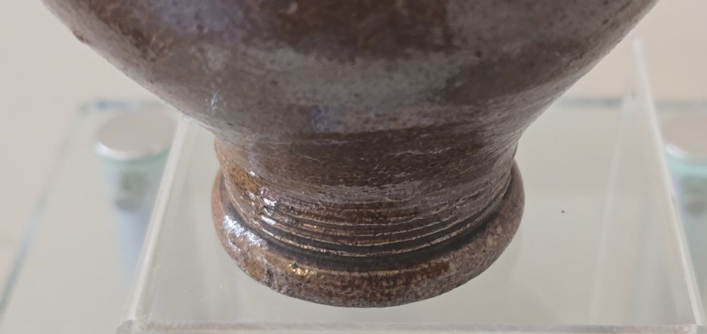 A 17th-century dark brown salt-glazed stoneware bottle featuring a bulbous body, narrow neck, turned base, and a single loop handle. View XV