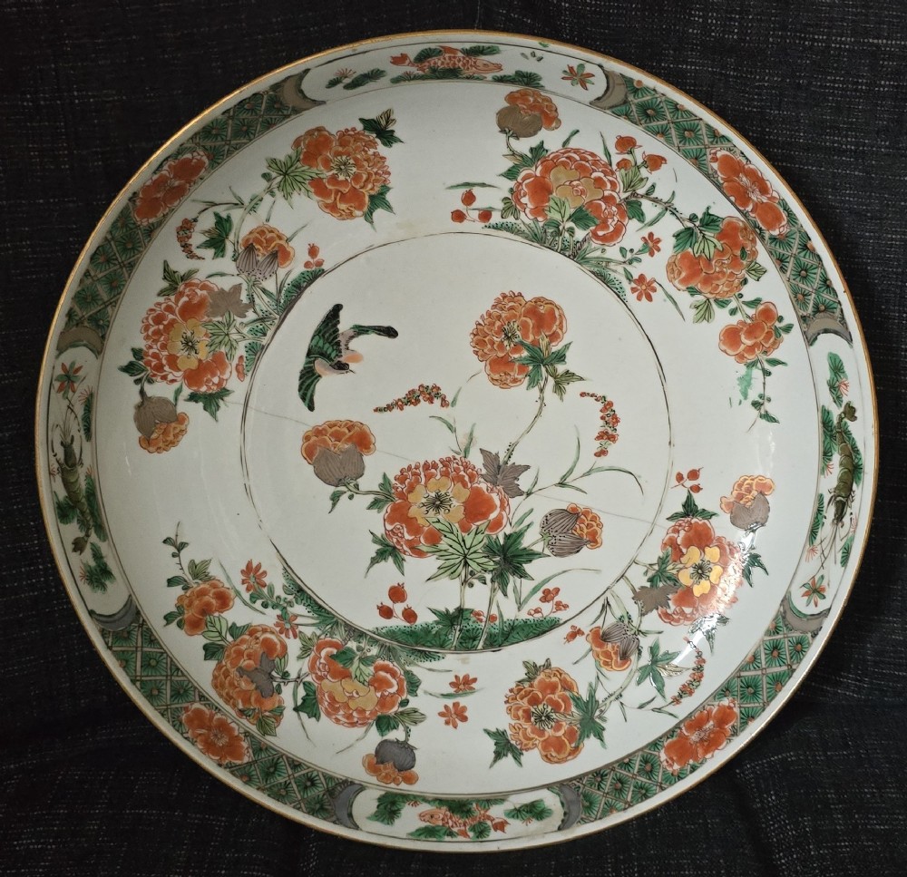 A circular Chinese famille verte porcelain dish featuring hand-painted peony blossoms, foliage, a bird in flight, and a decorative patterned border.