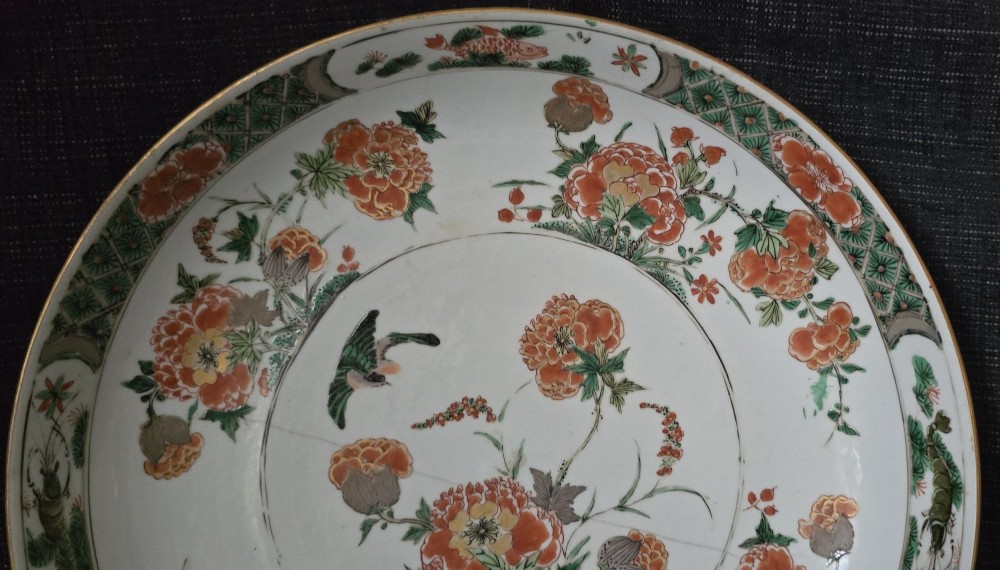 A circular Chinese famille verte porcelain dish featuring hand-painted peony blossoms, foliage, a bird in flight, and a decorative patterned border. View V