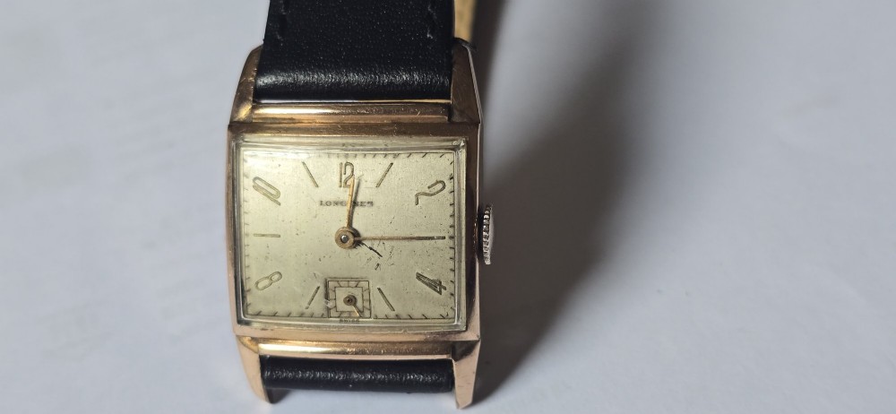 A vintage Longines rectangular wristwatch featuring a rose gold-filled case, patinated dial with Arabic numerals, sub-seconds register, and a black leather strap.