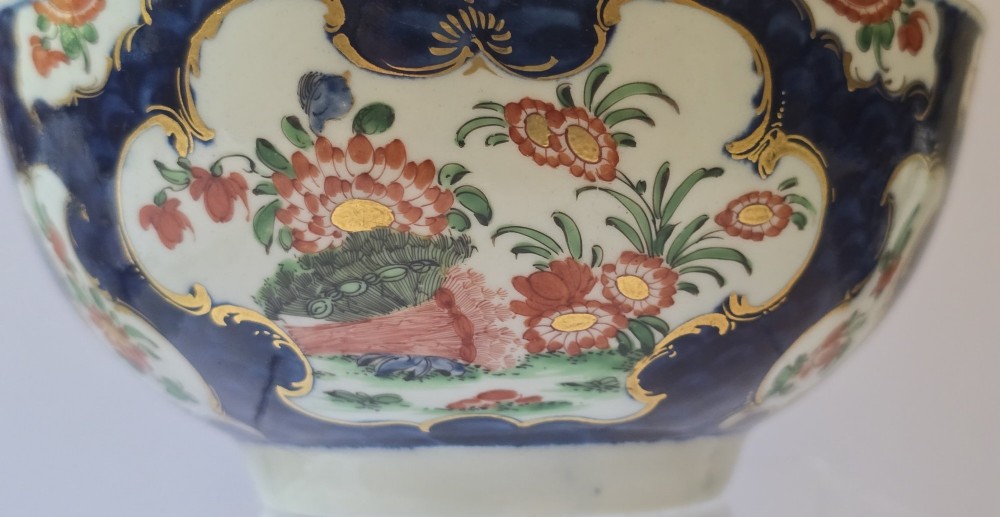 An eighteenth-century circular porcelain bowl featuring a blue scale ground, gilded rococo cartouches, and hand-painted Kakiemon floral panels. View II