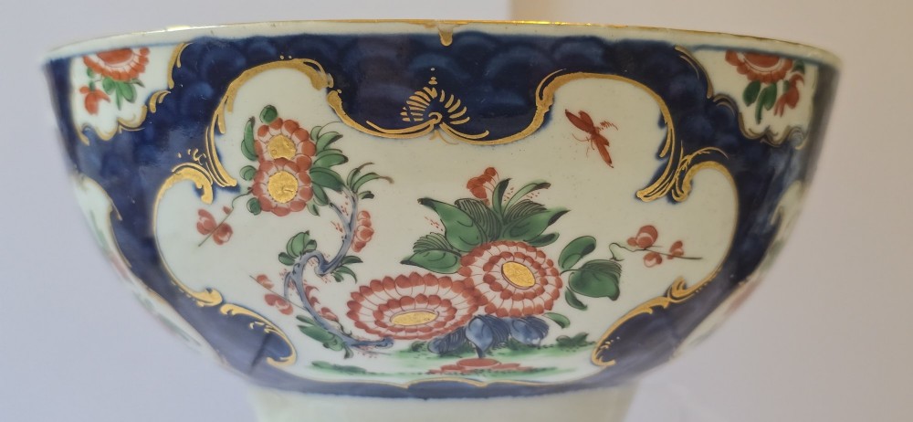 An eighteenth-century circular porcelain bowl featuring a blue scale ground, gilded rococo cartouches, and hand-painted Kakiemon floral panels. View V