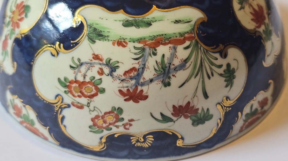 An eighteenth-century circular porcelain bowl featuring a blue scale ground, gilded rococo cartouches, and hand-painted Kakiemon floral panels. View VIII