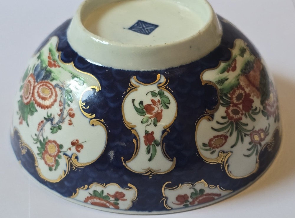 An eighteenth-century circular porcelain bowl featuring a blue scale ground, gilded rococo cartouches, and hand-painted Kakiemon floral panels. View XI