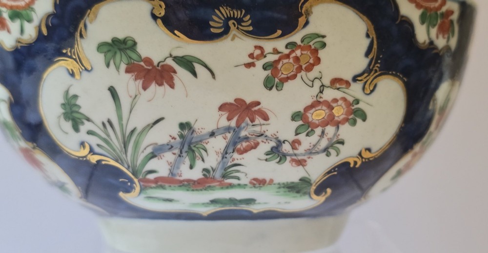 An eighteenth-century circular porcelain bowl featuring a blue scale ground, gilded rococo cartouches, and hand-painted Kakiemon floral panels. View XIII