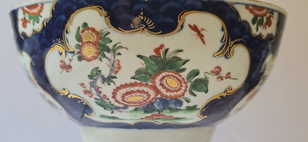 An eighteenth-century circular porcelain bowl featuring a blue scale ground, gilded rococo cartouches, and hand-painted Kakiemon floral panels. View XIV