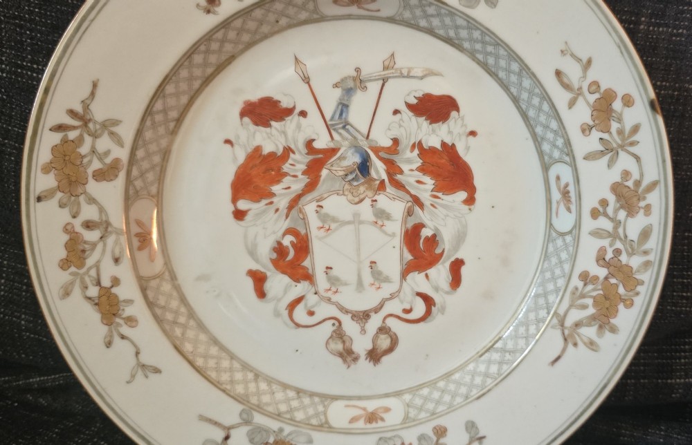 A circular Chinese export porcelain plate featuring a central heraldic crest with red mantling, encircled by a geometric diaper border and floral sprigs. View II