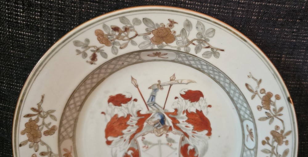 A circular Chinese export porcelain plate featuring a central heraldic crest with red mantling, encircled by a geometric diaper border and floral sprigs. View IV