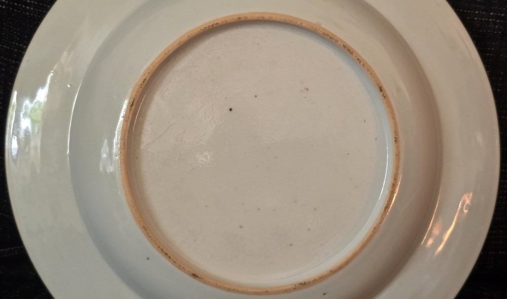 A circular Chinese export porcelain plate featuring a central heraldic crest with red mantling, encircled by a geometric diaper border and floral sprigs. View IX