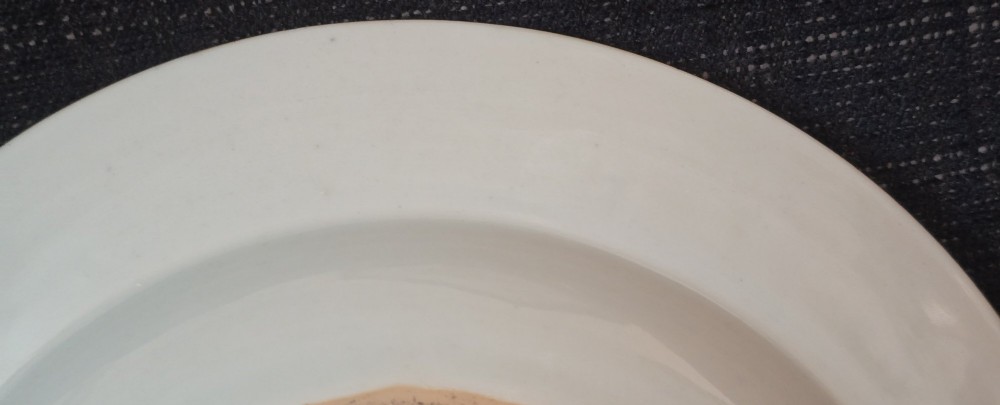 A circular Chinese export porcelain plate featuring a central heraldic crest with red mantling, encircled by a geometric diaper border and floral sprigs. View XII