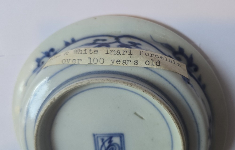 A circular Edo period Japanese Arita porcelain shallow dish featuring hand-painted cobalt blue underglaze figurative and floral decoration on an off-white ceramic body. View X