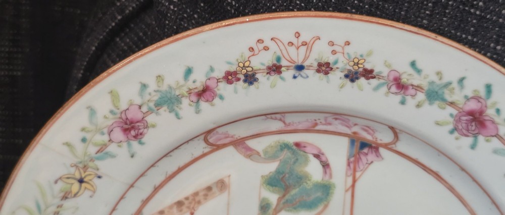 A pair of circular white porcelain plates hand-painted with famille rose enamels depicting figures in an interior and garden setting with a floral rim border. View XI