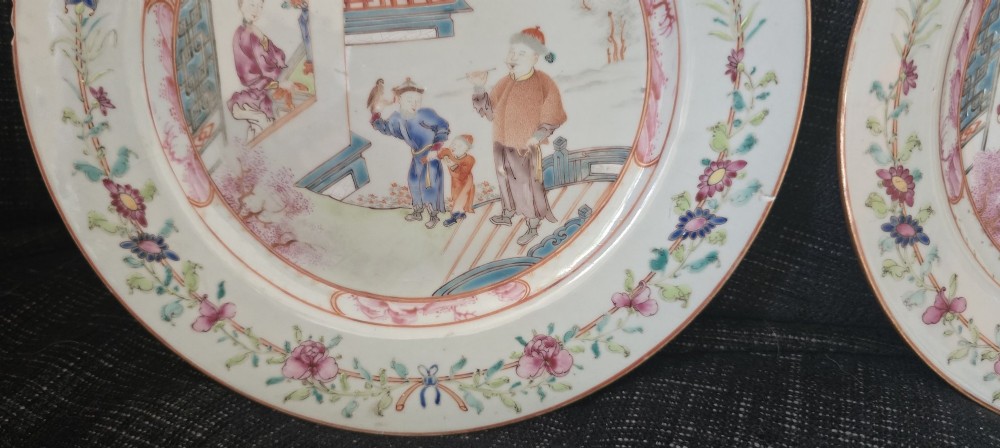A pair of circular white porcelain plates hand-painted with famille rose enamels depicting figures in an interior and garden setting with a floral rim border. View XIII