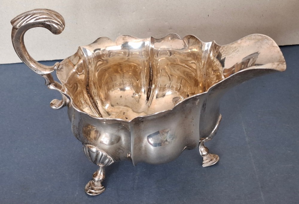A Victorian sterling silver sauce boat featuring a scalloped rim, a double-scroll handle, and three shell-capped feet.