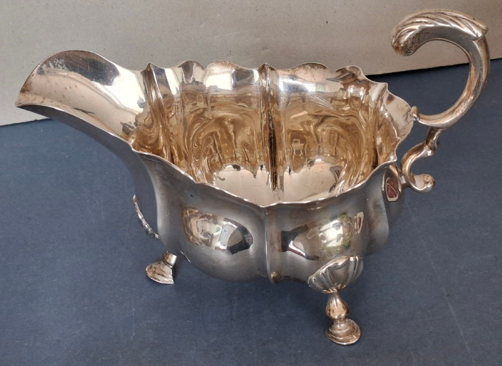 A Victorian sterling silver sauce boat featuring a scalloped rim, a double-scroll handle, and three shell-capped feet. View II