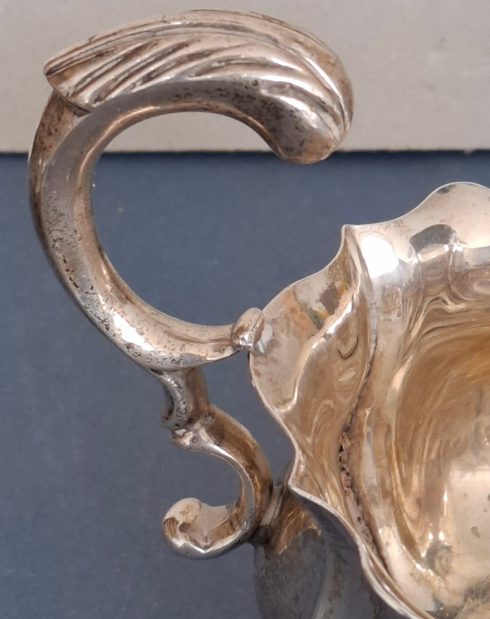 A Victorian sterling silver sauce boat featuring a scalloped rim, a double-scroll handle, and three shell-capped feet. View V