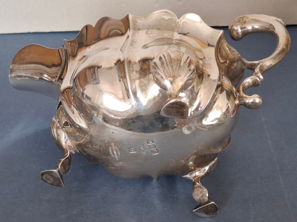 A Victorian sterling silver sauce boat featuring a scalloped rim, a double-scroll handle, and three shell-capped feet. View VIII