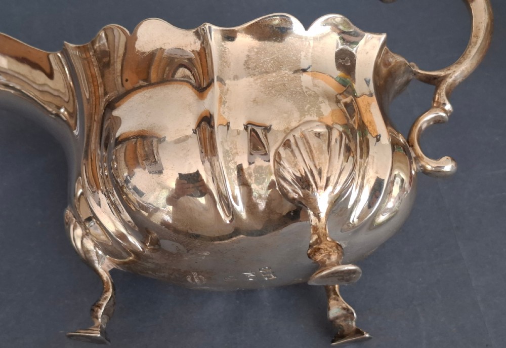 A Victorian sterling silver sauce boat featuring a scalloped rim, a double-scroll handle, and three shell-capped feet. View X