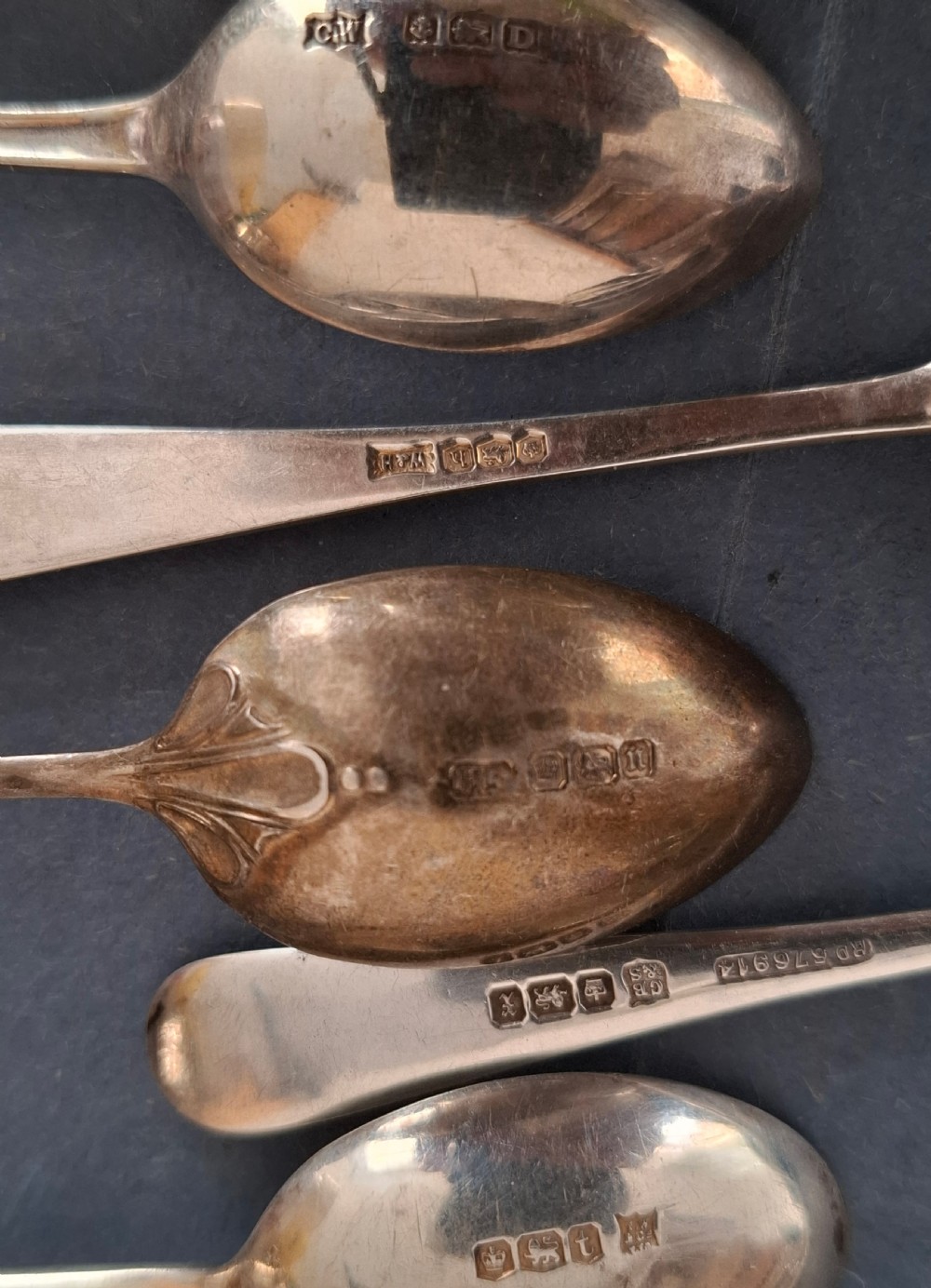 A collection of twenty-eight sterling silver tea and coffee spoons arranged in groups on a dark grey background. View IX