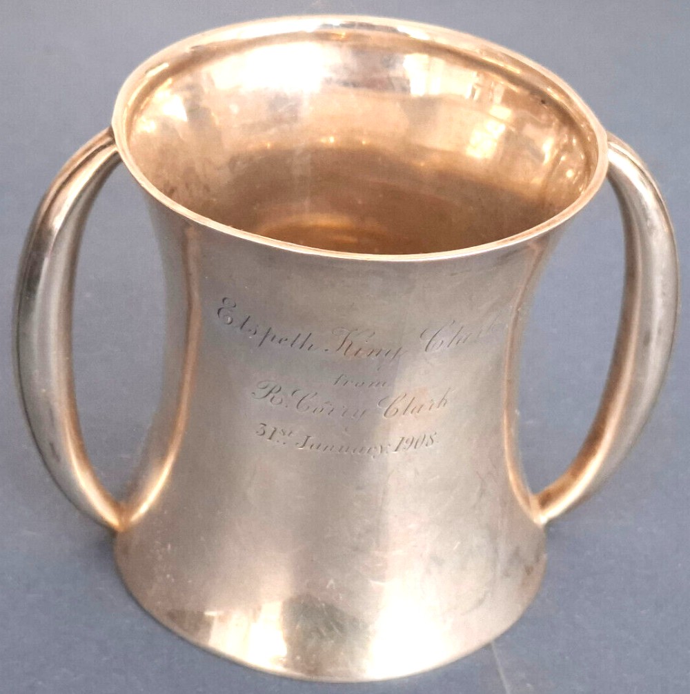 An Edwardian silver two-handled christening cup with a flared rim and base, featuring engraved cursive text on the front surface.