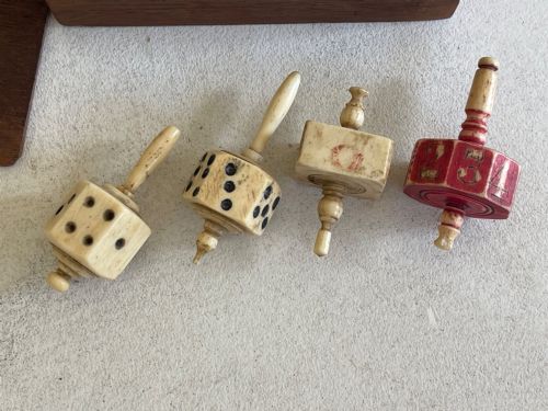 fig 1. A rectangular wooden box holding hand-carved bone teetotum spinning tops, miniature dice, and red and white counter discs.