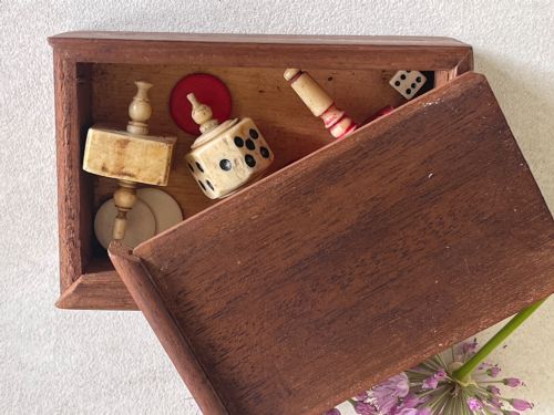 fig 2. A rectangular wooden box holding hand-carved bone teetotum spinning tops, miniature dice, and red and white counter discs.