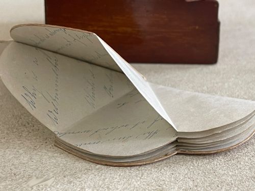 fig 3. An open small wooden box containing printed paper riddle slips set behind a heart-shaped printed card with floral motifs.