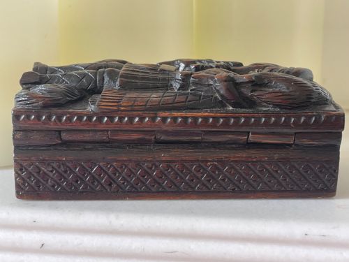 fig 1. A dark carved wooden table snuff box lid depicting a Scottish Highlander in a kilt carrying a stag across his shoulders with a hound at his feet.