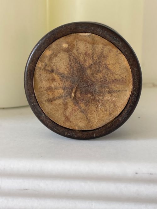 fig 3. A small turned dark wooden go-to-bed match holder featuring a cylindrical body, a moulded cap, and a match inserted in the centre top.